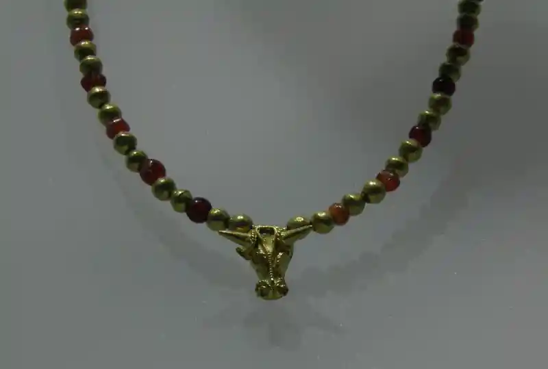 A gold necklace with red and gold beads and bullhead pendant A gold necklace with red and gold beads and bullhead pendant